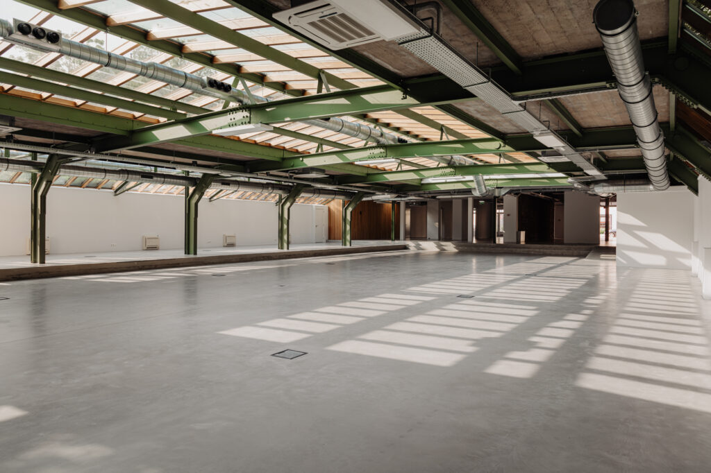 Lichte industriële ruimte met groene stalen balken en glazen dak aan de Plantage Middenlaan.